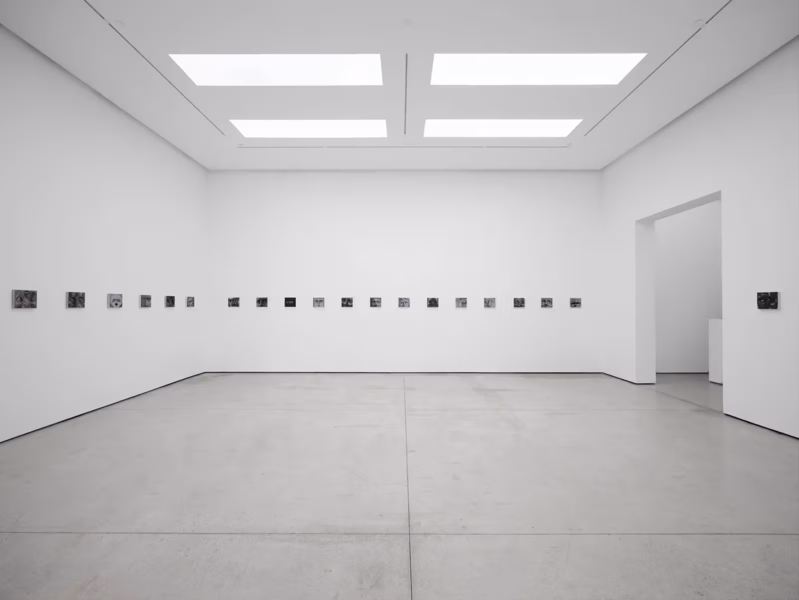 白色展间墙面横向排列小幅灰阶面容作品，中间穿插深色日期画板