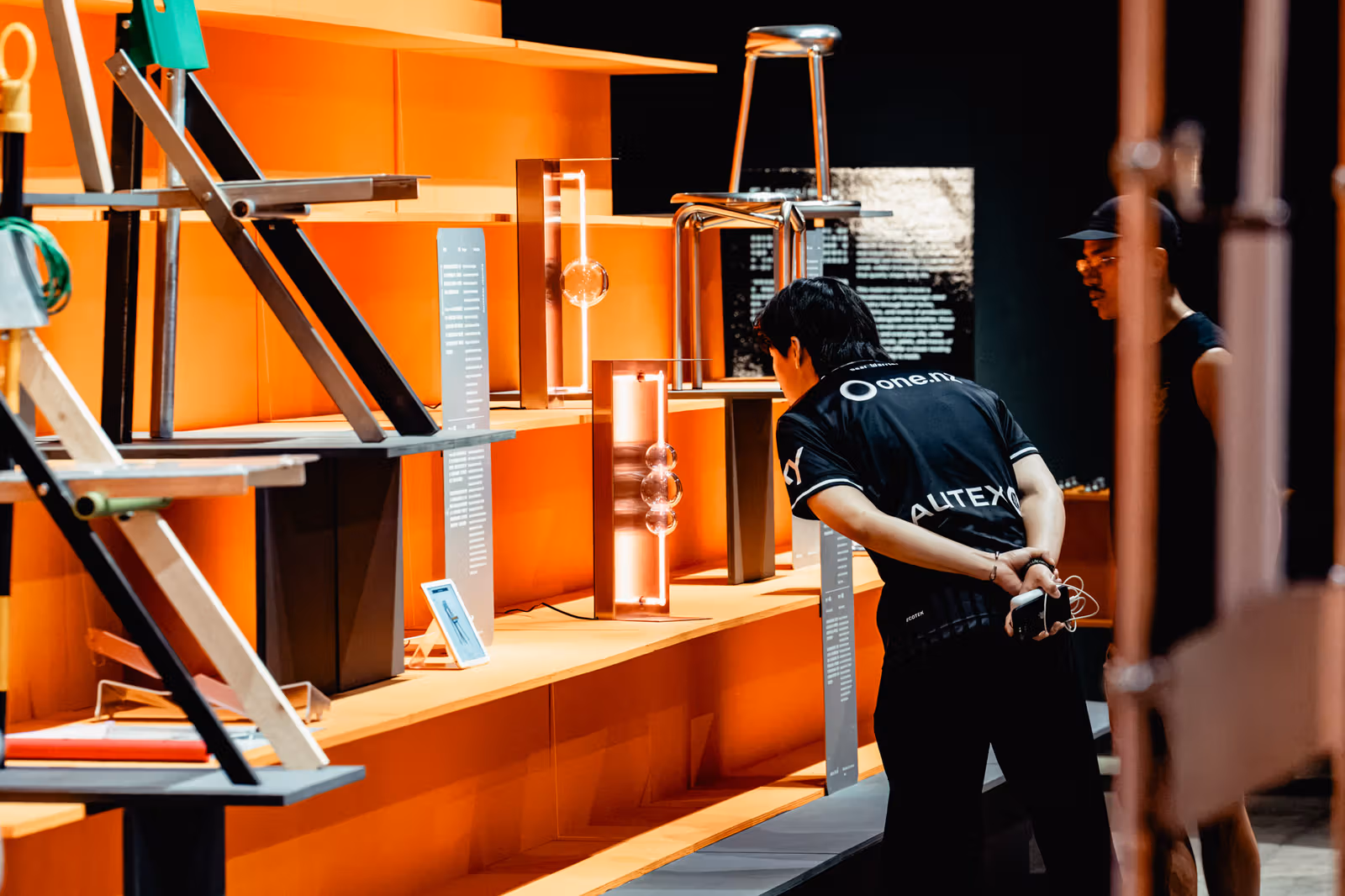 オレンジ色の展示台の椅子や縦長の物を二人の来場者が近くで見ている