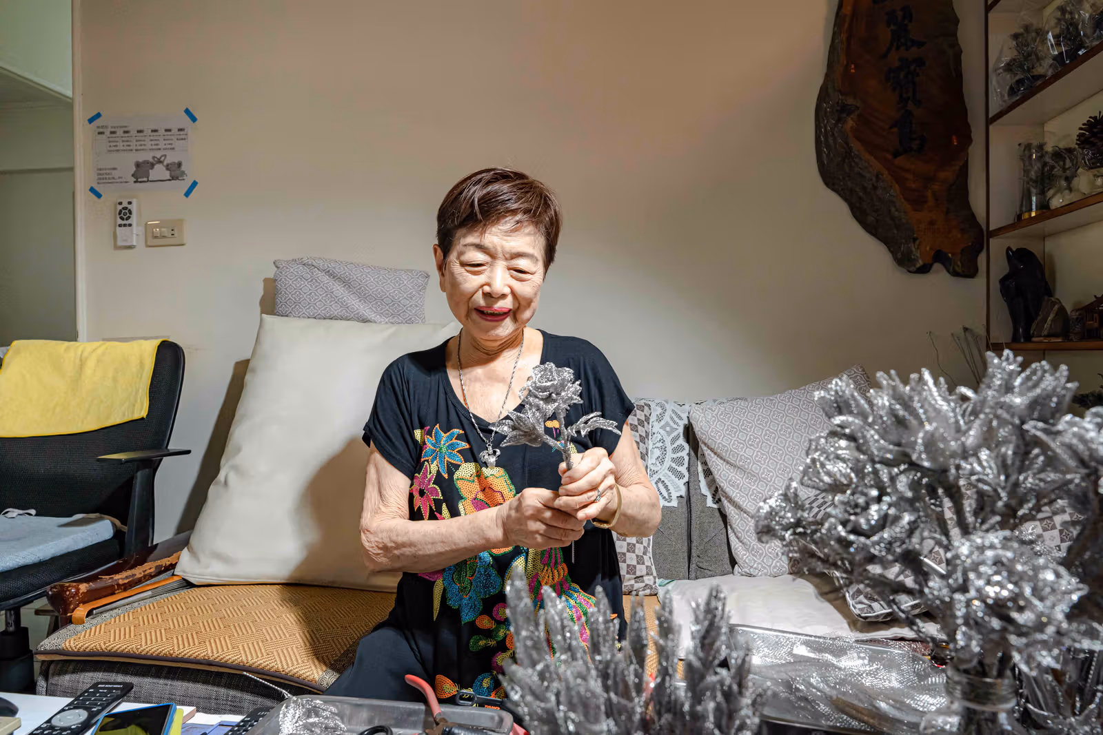 座った林洪玉秀が銀色の金属の花を持ち、手前と右側にも金属の花が並ぶ
