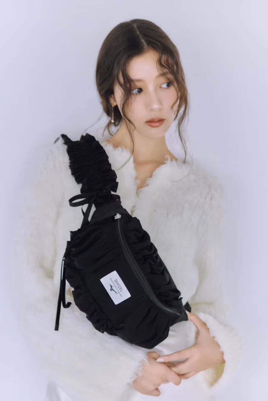 白いトップスのモデルが、ギャザー入りストラップと白いダブルロゴの付いた黒いバッグを斜め掛け。